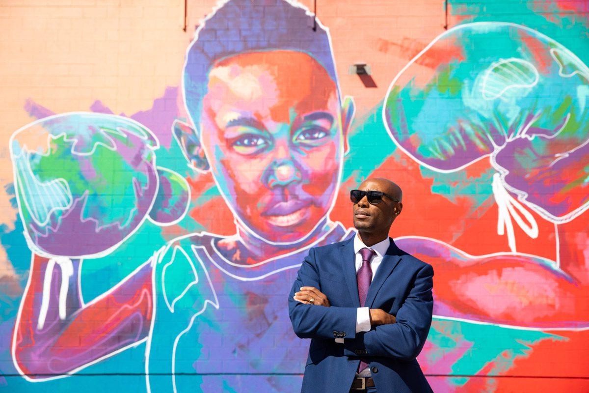 密歇根州立大学丹佛 alumnus Eric Williams standing in front of street art of a boy with boxing gloves on his hands.
